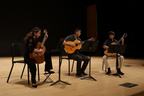 A guitar trio seated, playing