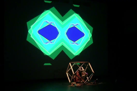 Performer in small cage with projections on wall