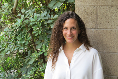 Person with curly hair in front of shrubs